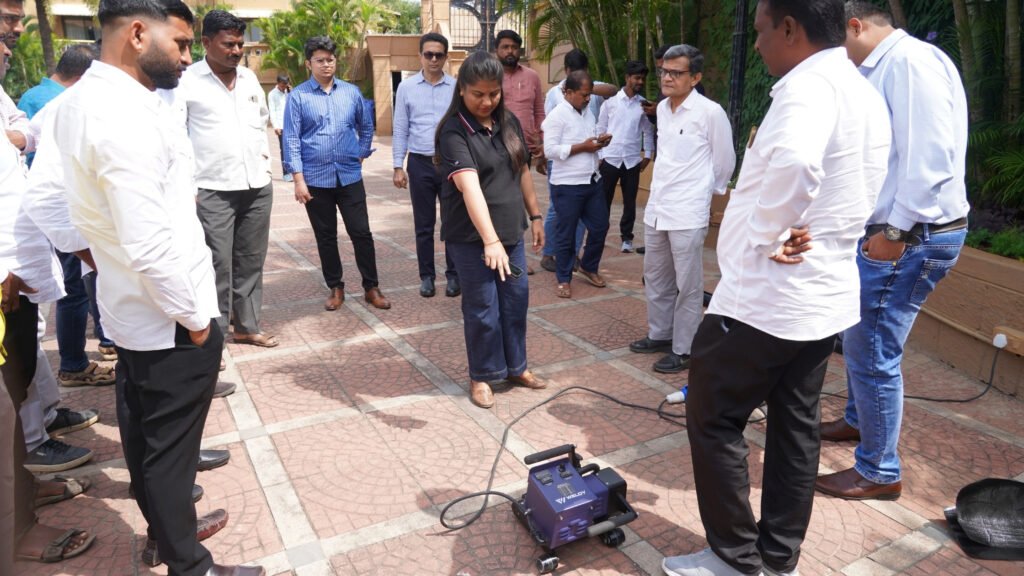 Trainer demonstrating a Weldy geomembrane welding machine to installers and participants during the outdoor practical session at GeoWeld Connect 2025.