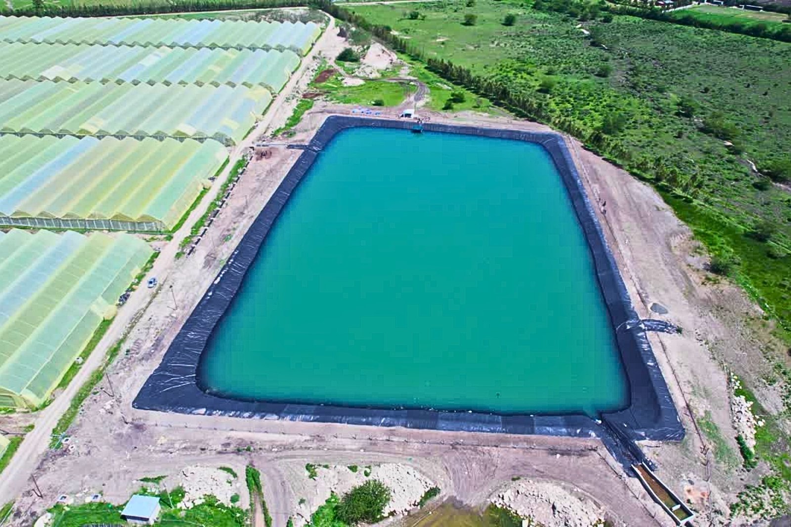 HDPE geomembrane pond liner installed for farm water storage near greenhouse.